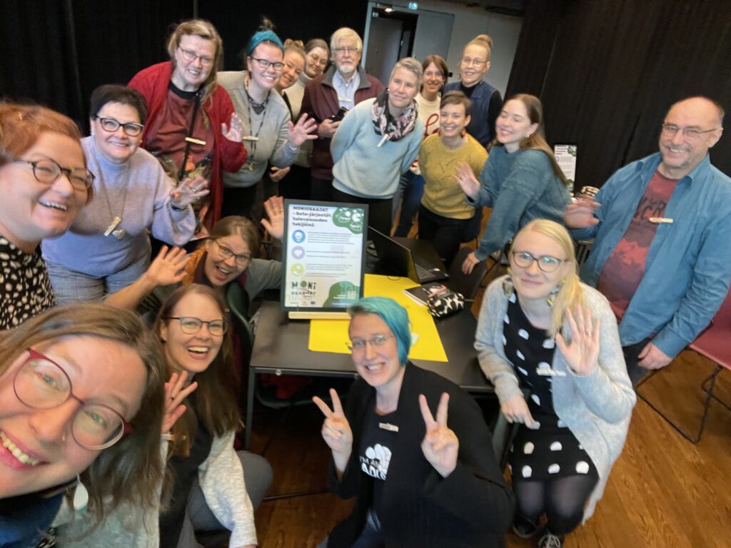 Viestintätyöpajan osallistujat ryhmäkuvassa hymyilemässä ja vilkuttelemassa. 