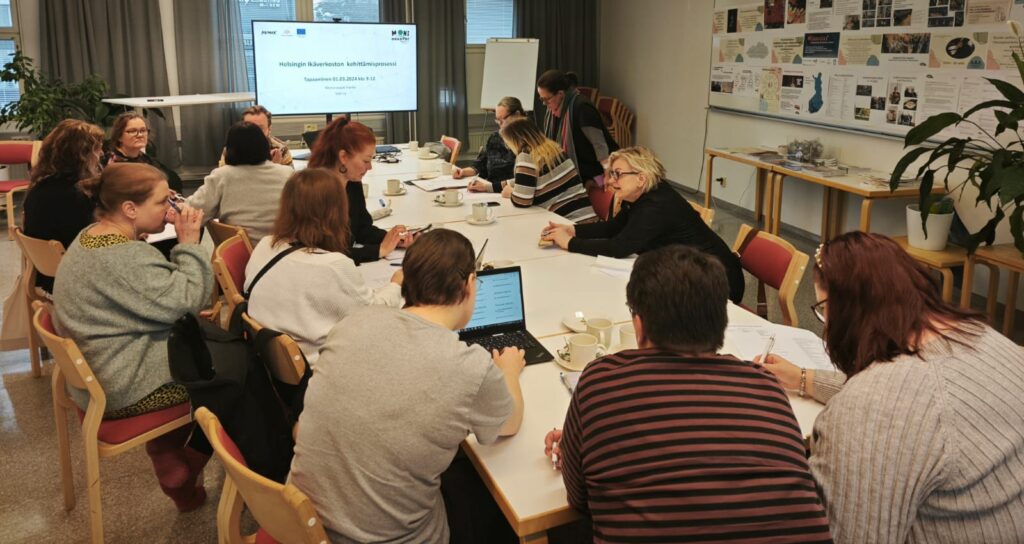 Kuvassa ihmisiä työskentelee ryhmissä pitkän kokouspöydän ääressä.