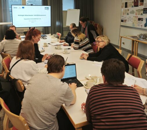 Kokouspöydän ääressä työskentelee ihmisiä pienryhmissä.